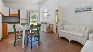Cocina funcional con armarios blancos, una mesa de comedor con sillas y un sofá blanco en un ambiente luminoso con vistas.