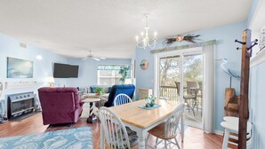 A spacious living room with a wooden dining table, a fireplace, and a large window. - Sunset Retreat 2 Bedroom Pet-Friendly Condo at Oyster Point (Kill Devil Hills)