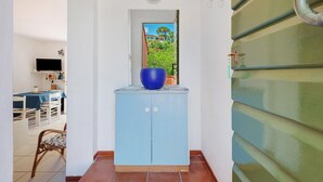 Een gang met een blauwe kast, een televisie op een tafel en uitzicht op groen buiten.