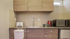 Cucina con mobili in legno, lavello in acciaio inossidabile, microonde, bollitore e un piccolo frigorifero.