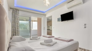Ein Hotelzimmer mit zwei Betten, einem Flachbildfernseher, einer Klimaanlage und einer Glastür zu einem Balkon.