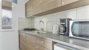 Eine moderne Küche mit Holzschränken, einer Edelstahl-Spüle, einer Kaffeemaschine und einer Mikrowelle.