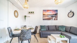 A modern living room with a dining area, a gray sofa, a white table, and a wall clock. - Apartment "Casa Verde" with Mountain View, Shared Pool & Wi-Fi (Roldán)