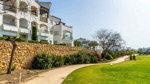 A residential area with a stone wall, a curved pathway, and modern houses with balconies. - Apartment "Casa Verde" with Mountain View, Shared Pool & Wi-Fi (Roldán)
