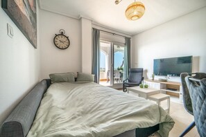 A modern bedroom with a bed, a television, a desk with a chair, and a balcony with a view. - Apartment "Casa Verde" with Mountain View, Shared Pool & Wi-Fi (Roldán)