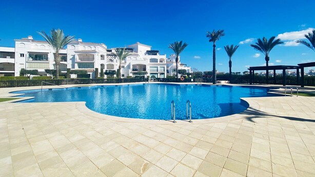 A swimming pool with a tiled deck, surrounded by palm trees and a building with balconies. - Apartment "Casa Verde" with Mountain View, Shared Pool & Wi-Fi (Roldán)