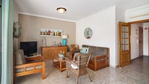 A living room with a television, sofa, wicker chair, and a wooden coffee table. - Apartment "Columbus Beach" with Sea View, Shared Pool & Wi-Fi (Quarteira)
