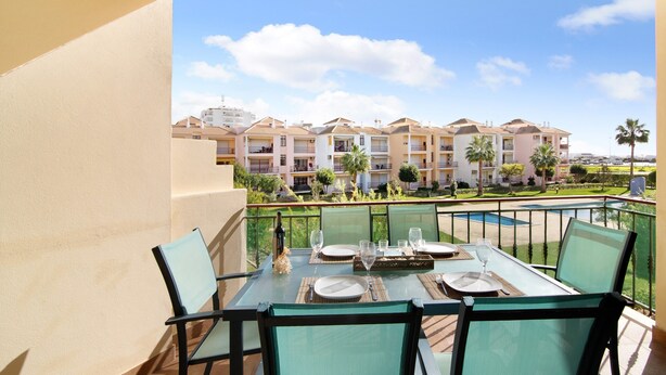 A balcony with a table set for dining, overlooking a pool and a row of buildings. - Apartment "Columbus Beach" with Sea View, Shared Pool & Wi-Fi (Quarteira)
