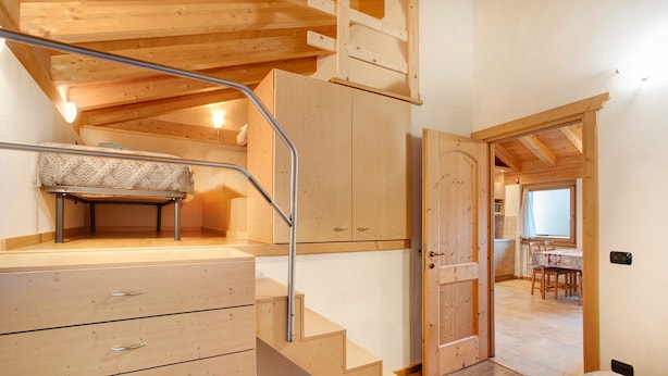 Un escalier en bois mène à une chambre aménagée en mezzanine, où se trouvent un lit, un bureau et une fenêtre.