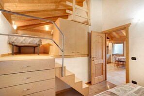 A wooden staircase leading to a loft bedroom with a bed, a desk, and a window.
