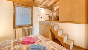 Une chambre à coucher avec un lit, une fenêtre avec des rideaux, un escalier en bois et une armoire.
