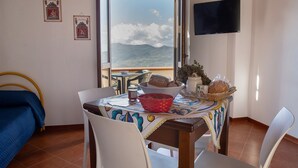 A room with a dining table, chairs, a bed, a TV, and a view of mountains. - Holiday Home 'Paese Albergo - Arconides' with Sea View, Balcony and Wi-Fi (Motta D'affermo)