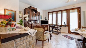 Un comedor con una mesa de madera, sillas, un televisor y una zona de cocina con armarios y una cesta de frutas.