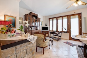 A dining area with a wooden table, chairs, a television, and a kitchen area with cabinets and a fruit basket.