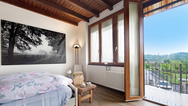 Un dormitorio con cama, una mesita de noche con lámpara, un ventanal y vistas al exterior.