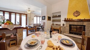 Un comedor con chimenea, una mesa dispuesta con platos, vasos y cubiertos, y vista del salón comedor al fondo.