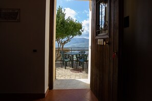 An open door leading to an outdoor patio with a table and chairs, a tree, and a view of mountains. - Holiday Home "Paese Albergo - Athena" with Sea View, Balcony and Wi-Fi (Motta D'affermo)