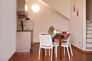 Un coin repas avec une table, des chaises, une petite plante et une cuisine en arrière-plan.