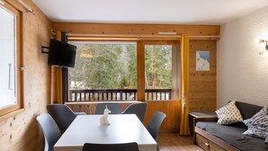 Une cabane en bois comprenant une table à manger, des chaises, un canapé, un téléviseur fixé au mur et une fenêtre donnant sur les arbres.