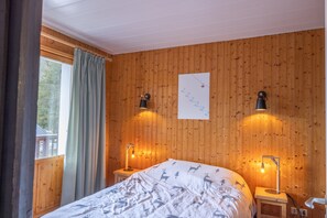 Une pièce aux murs lambrissés, comprenant un lit, deux lampes de chevet, une fenêtre avec des rideaux et un panneau fixé au mur.