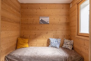 Ein Zimmer mit Holzwänden, einem Bett, einem Fenster und einem Bild an der Wand.