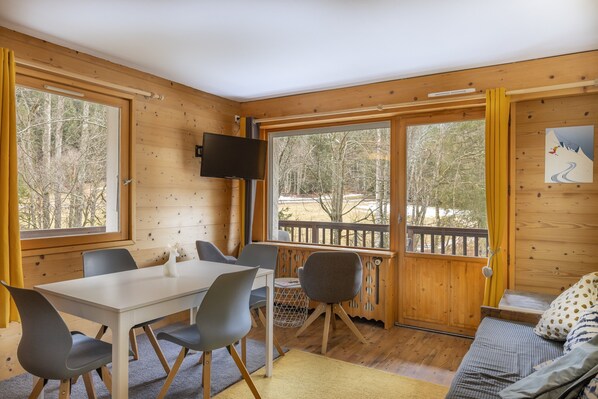 Une cabane en bois comprenant un coin repas, un canapé et un téléviseur fixé au mur.