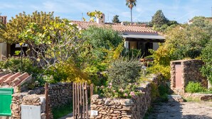 A rustic stone wall with a wooden gate, a stone pathway, and a building with a tiled roof surrounded by lush greenery and trees. - three-room apartment in pine forest two bathrooms (Baia Sant'Anna)