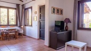 A room with a dining table, chairs, a TV on a cabinet, and a small white table. - three-room apartment in pine forest two bathrooms (Baia Sant'Anna)