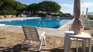 A pool area with lounge chairs and umbrellas, surrounded by trees and a clear sky. - three-room apartment in pine forest two bathrooms (Baia Sant'Anna)