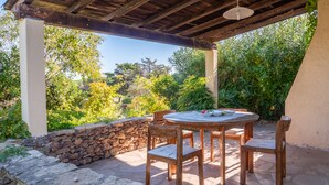 A covered outdoor patio with a round wooden table and chairs, surrounded by stone walls and lush greenery. - three-room apartment in pine forest two bathrooms (Baia Sant'Anna)