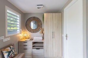 A room with a window, a mirror, a lamp, a wardrobe, and a bedside table.