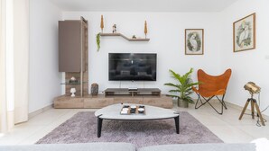 Una sala de estar moderna con televisor de pantalla plana, una mesa de centro, un sofá, una silla, una planta y obras de arte en las paredes.