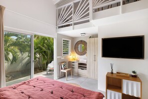 A modern bedroom with a large bed, a TV, and a balcony with a view of palm trees.