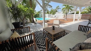 Un espacio al aire libre cubierto con piscina, sillones de descanso y plantas en macetas.