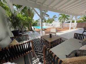 A covered outdoor seating area with a pool, lounge chairs, and potted plants.