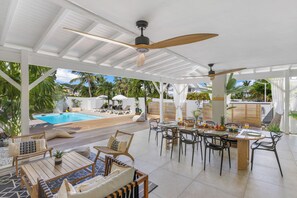 A covered outdoor area with a pool, lounge chairs, and a dining table set for breakfast.