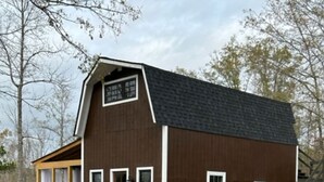 A modern barn-style building with a sloped roof, large windows, and a covered porch area.