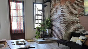 A spacious living area with a brick wall, a black sofa, a dining table, and a staircase.