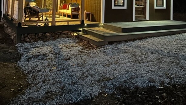 A small, dark-colored wooden house with a sloped roof, large windows, and a covered porch area.