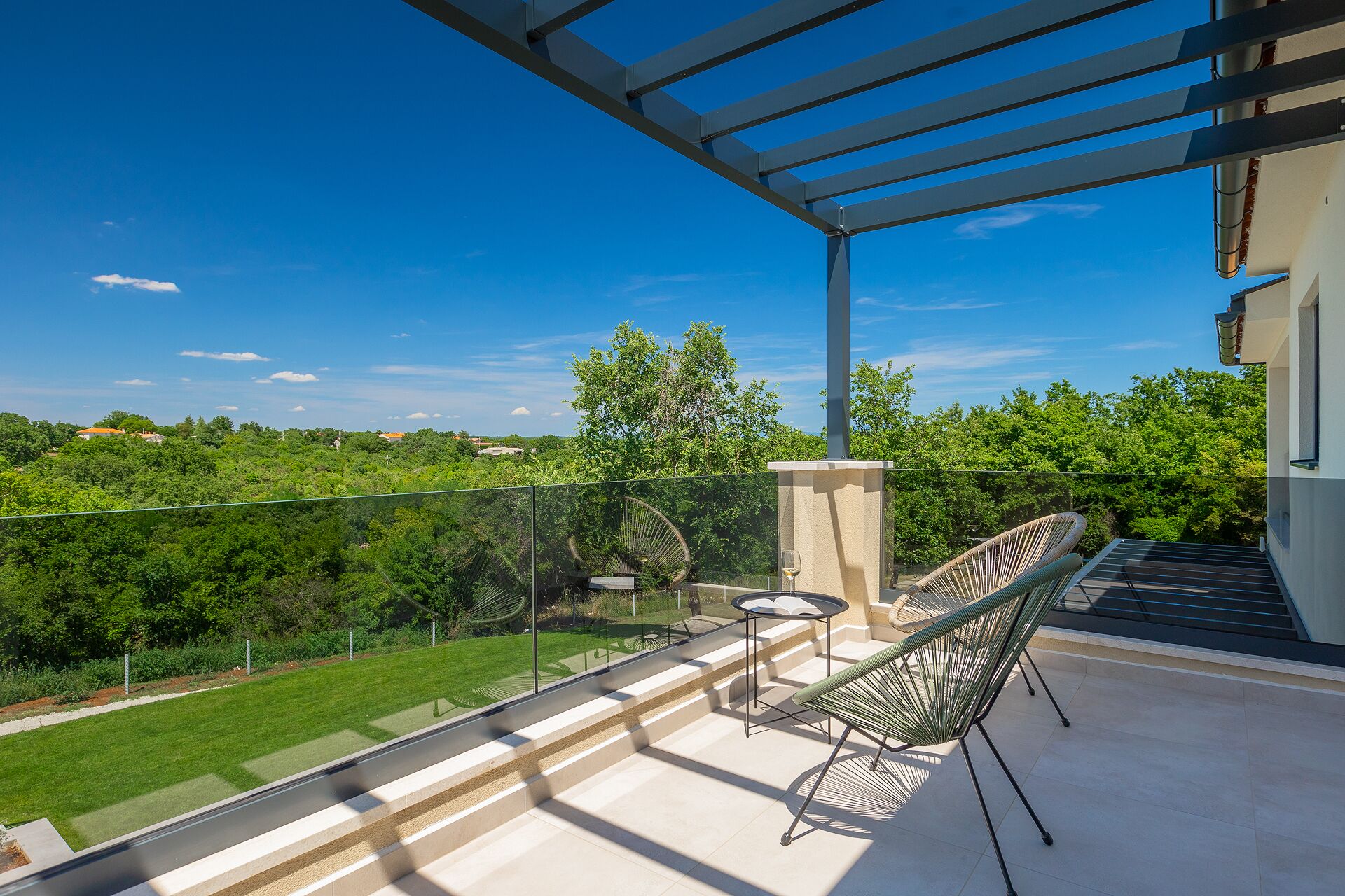 A balcony with a pergola, outdoor furniture, and a view of greenery and distant buildings.