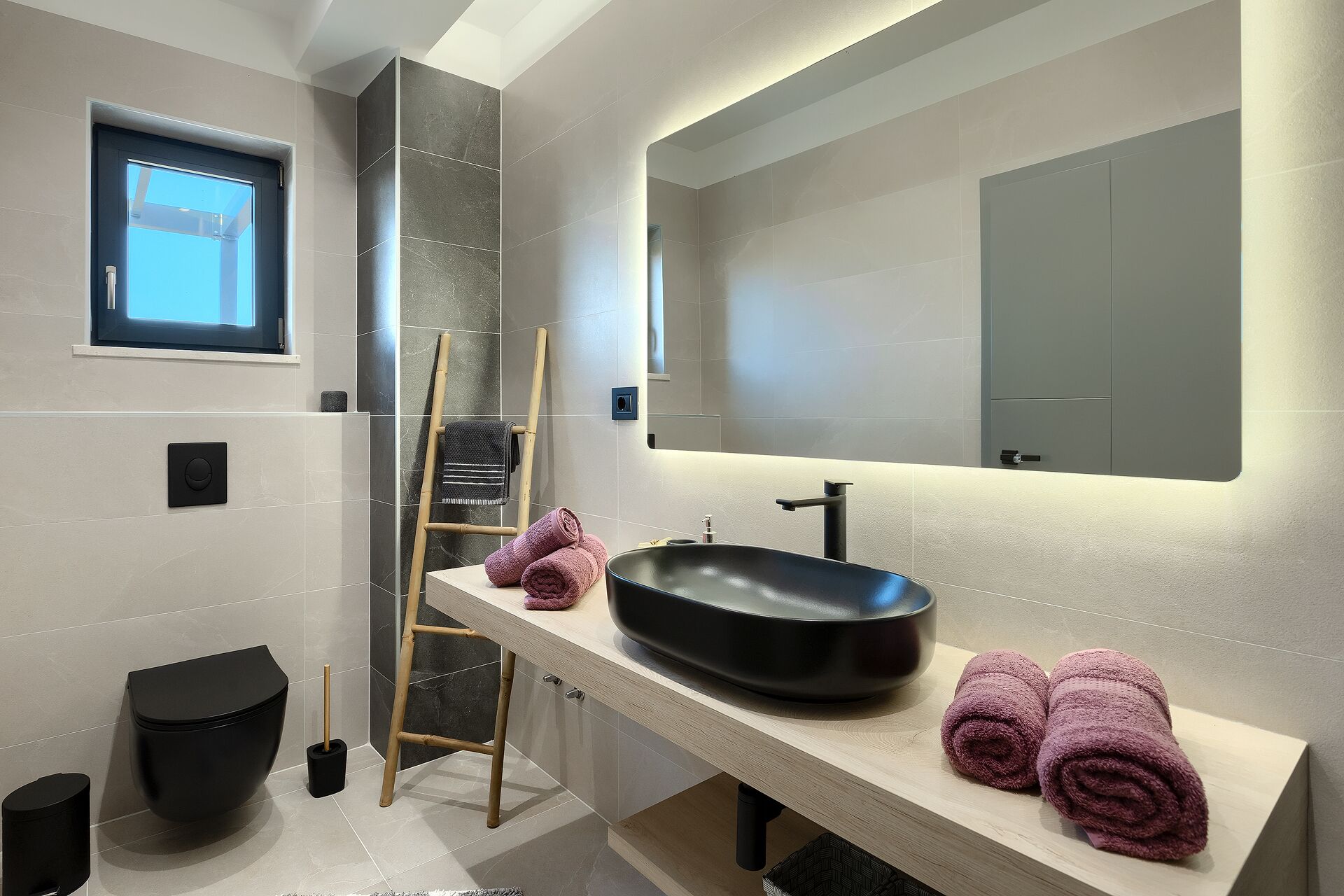 A modern bathroom with a black sink, a mirror, and a window.