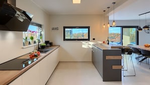 A modern kitchen with a central island, a window with a view, and a dining area with a table and chairs. - In a Small Village Surrounded by Nature (Barban)