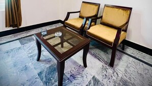 A room with two wooden chairs with cushioned seats, a glass-top coffee table, and a patterned marble floor. - Apple Hotel and Restaurant (Timergara)