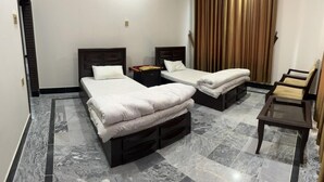 A hotel room with two beds, a small table, and a chair. - Apple Hotel and Restaurant (Timergara)