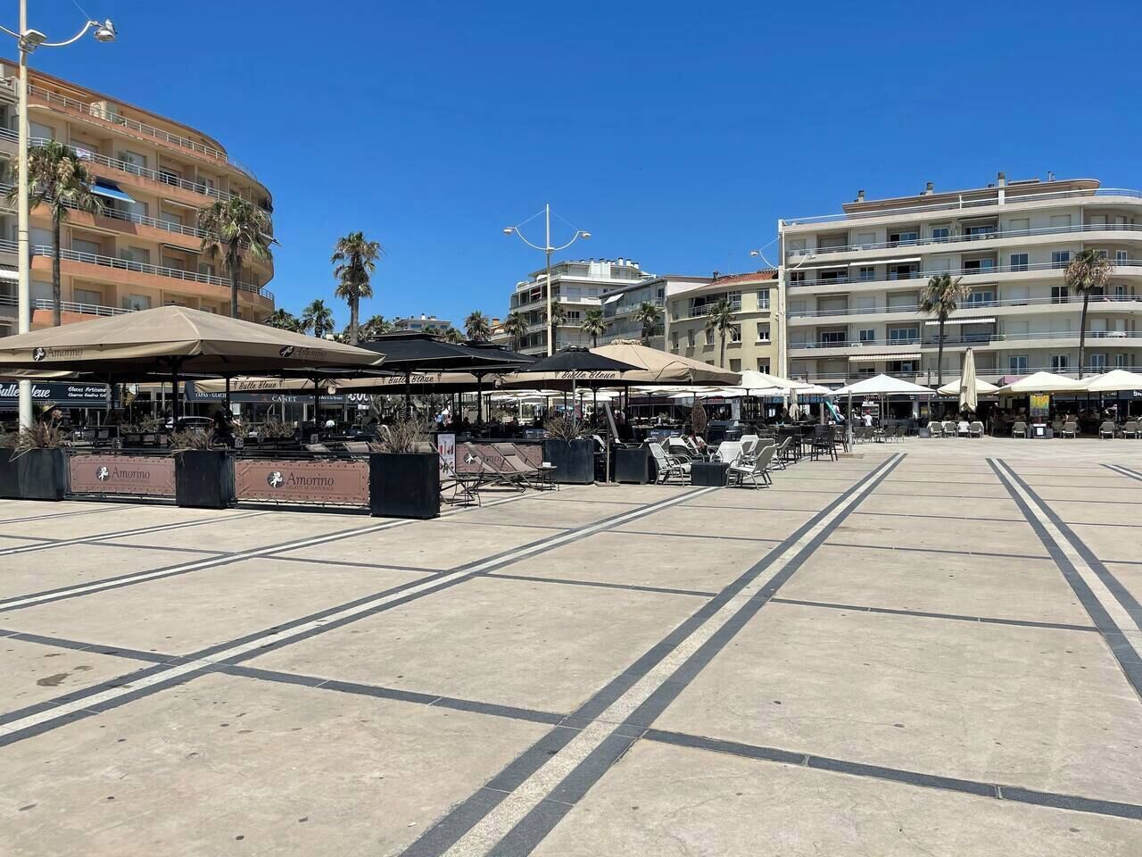 An outdoor plaza with seating areas, palm trees, and buildings in the background.