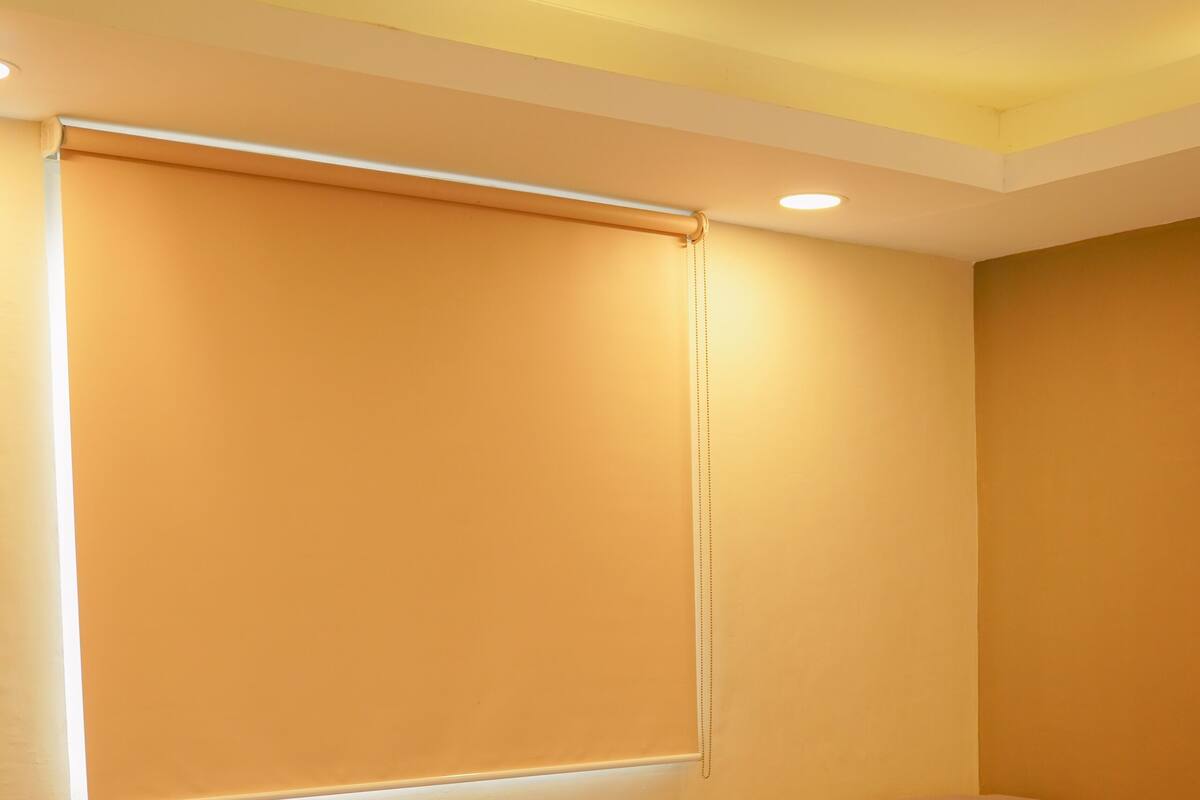 A room with two beds, each with a mattress and pillows, and a large window with blinds.