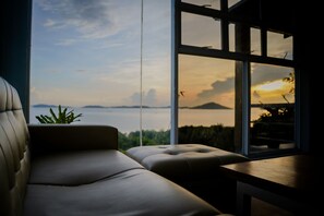 A modern interior with a sofa and a table near a large window overlooking a body of water and distant landscape. - Mamima BnB (Caramoan)