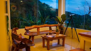Un interior moderno con un banco y una mesa de madera, un telescopio y vistas a zonas verdes a través de grandes ventanales.
