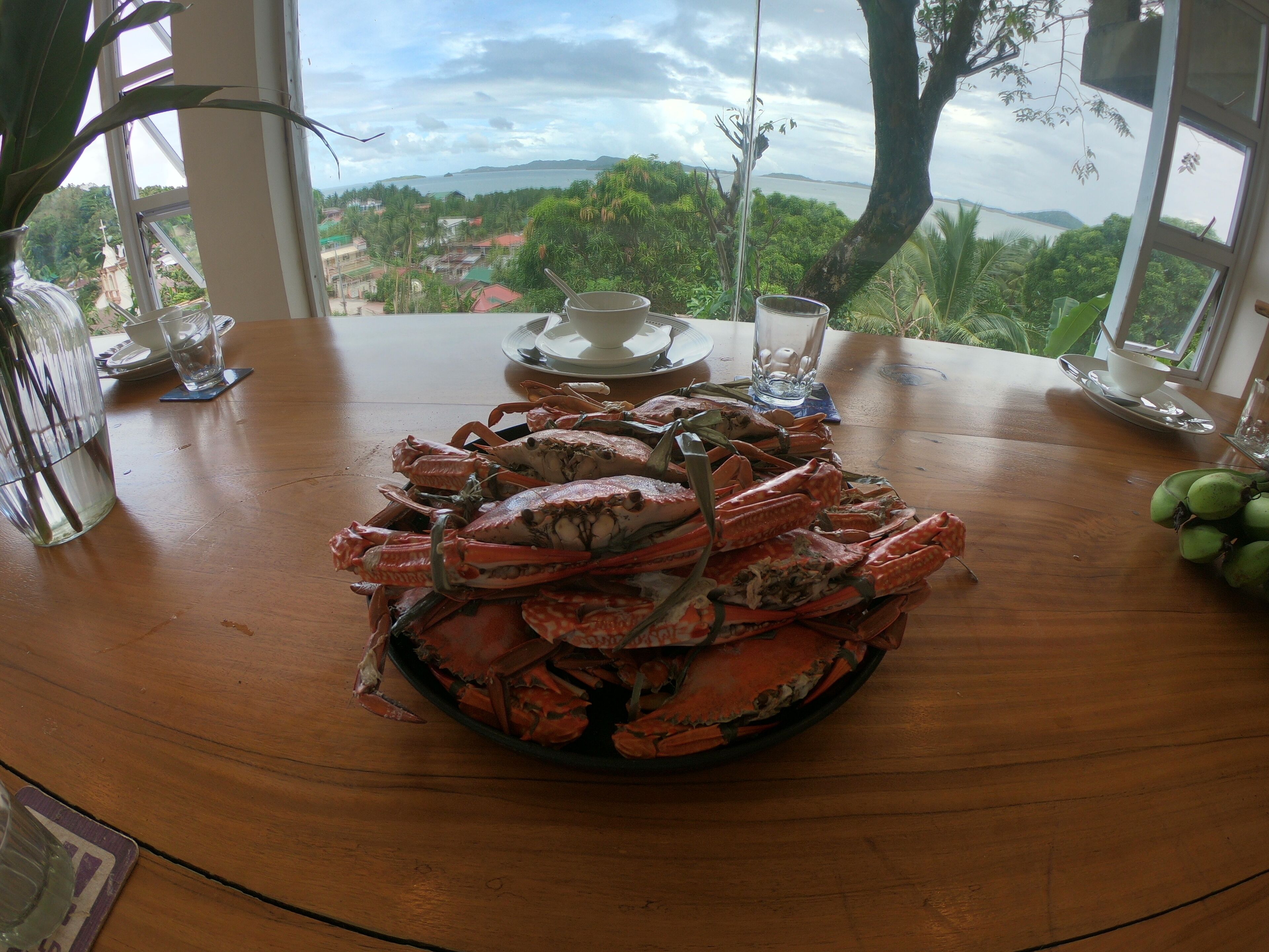 A dining table with a large bowl of cooked crabs, a glass of water, and a cup on a saucer.