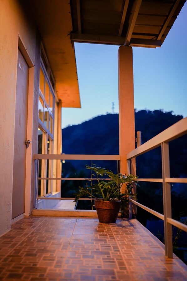 A balcony with a tiled floor, potted plants, and a view of a mountain at dusk. - Mamima BnB (Caramoan)
